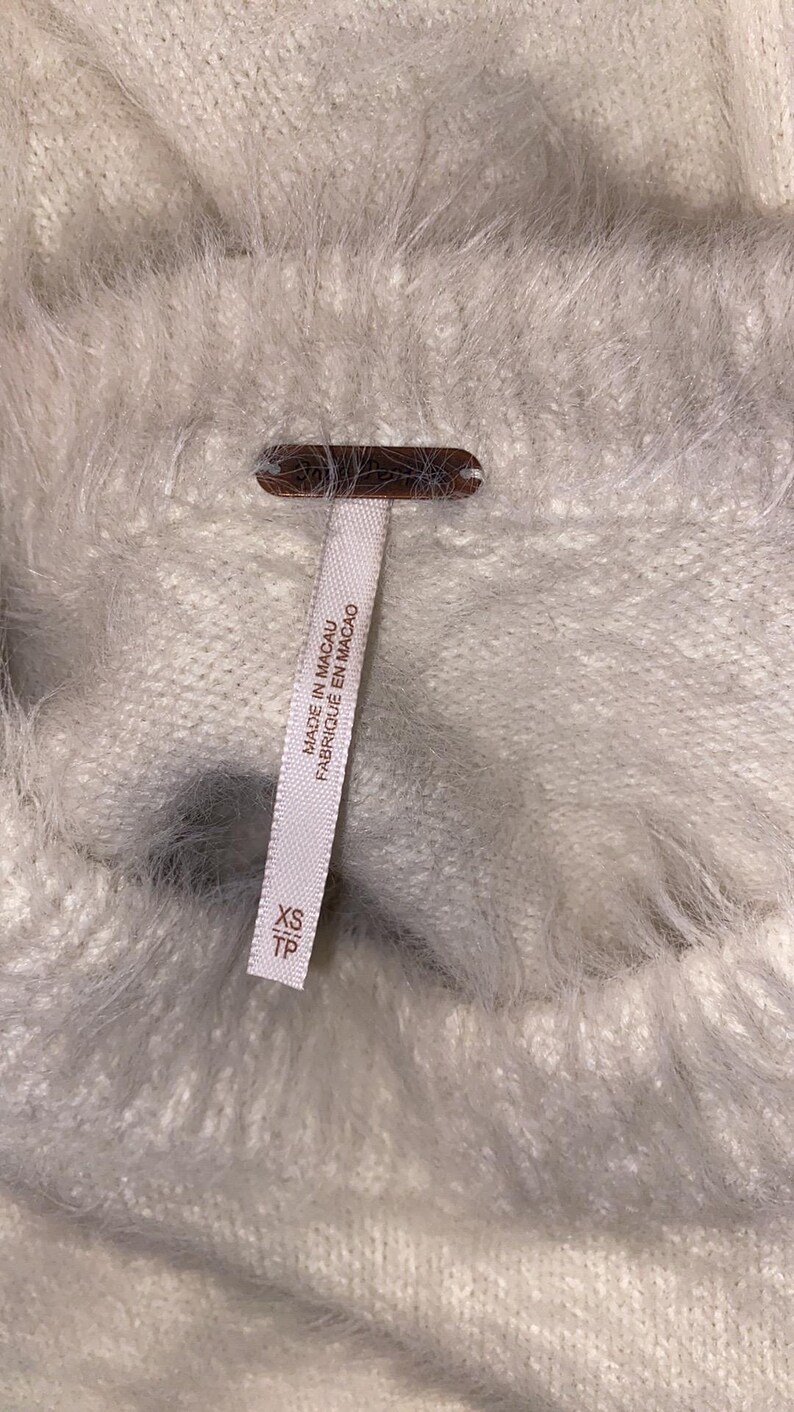 May include: White fuzzy sweater with a tag that reads "Made in Macau Fabrique en Macao" and "XS TP".