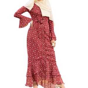 May include: A long, burgundy dress with a white polka dot pattern. The dress features long sleeves with flared cuffs, a belted waist, and a tiered, ruffled skirt. A beige headscarf is worn with the dress.