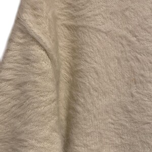 May include: Close-up of a white fuzzy sweater with a soft, textured knit.