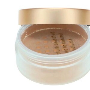 May include: A clear, round cosmetic jar with a gold-colored lid. The jar contains a light beige powder. Text on the powder reads "texture selected, es to control, volume".