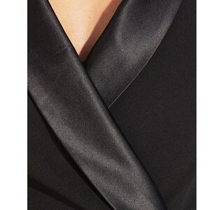 May include: A black satin collar on a black blazer. The collar is folded over and has a sharp crease.