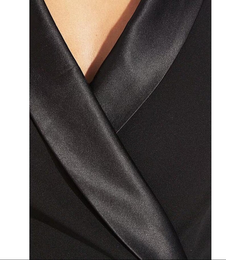 May include: A black satin collar on a black blazer. The collar is folded over and has a sharp crease.