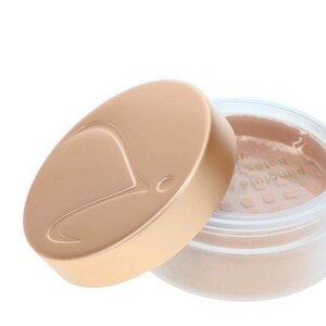 May include: A beige powder makeup product in a clear jar with a matching lid. The lid is off, revealing the powder inside. The lid has a curved design and a logo. The product is likely for the face.