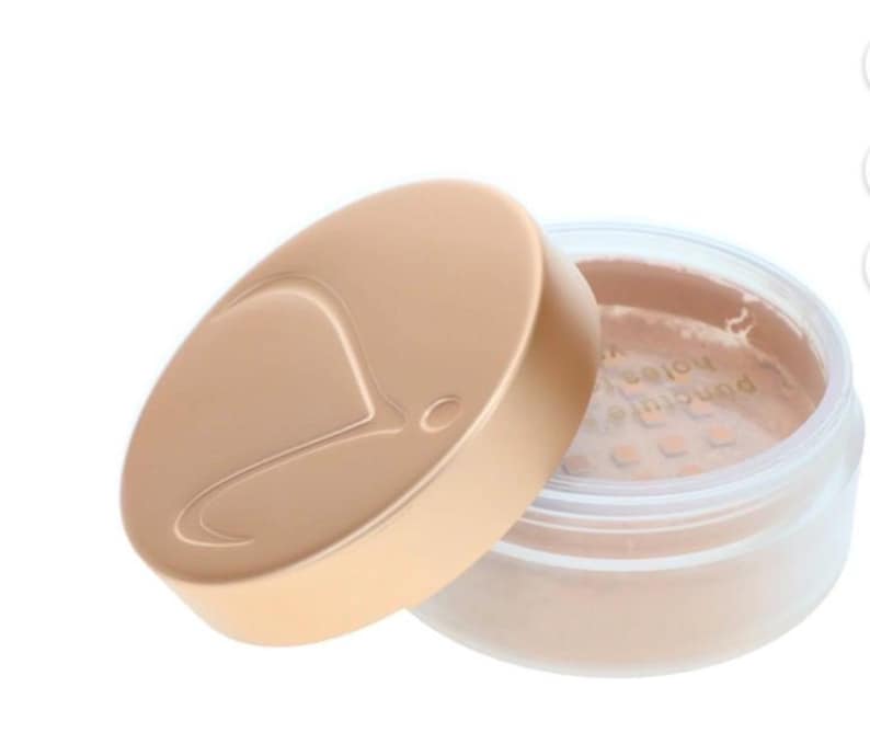May include: A beige powder makeup product in a clear jar with a matching lid. The lid is off, revealing the powder inside. The lid has a curved design and a logo. The product is likely for the face.
