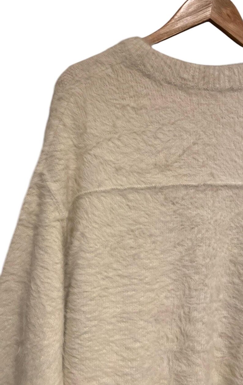 May include: A white fuzzy sweater with a crew neck and long sleeves.