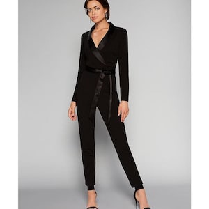 May include: A black jumpsuit with a satin trim collar and a matching satin sash. The jumpsuit has long sleeves and a wrap-style bodice.