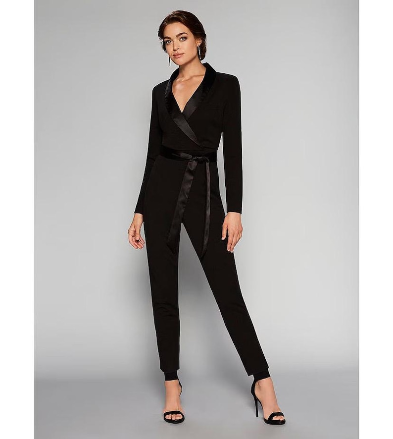 May include: A black jumpsuit with a satin trim collar and a matching satin sash. The jumpsuit has long sleeves and a wrap-style bodice.