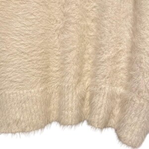 May include: A close-up of a soft, fluffy, white fabric with a fuzzy texture. The fabric is folded and has a slightly wavy edge.