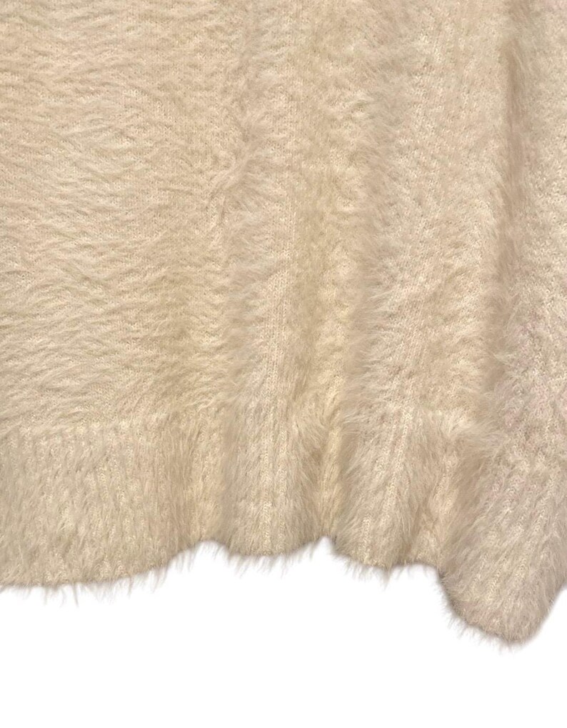 May include: A close-up of a soft, fluffy, white fabric with a fuzzy texture. The fabric is folded and has a slightly wavy edge.