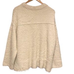 May include: A fluffy white sweater with a crew neck and long sleeves. The sweater has a slightly oversized fit and a relaxed silhouette.