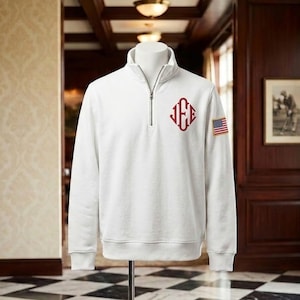May include: A white quarter-zip pullover sweatshirt featuring a red embroidered monogram with the letters JFE on the left chest and a small rectangular American flag patch on the right sleeve, displayed on a mannequin torso.