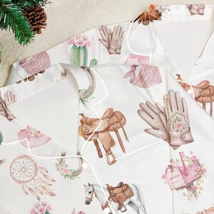 Puede incluir: Camiseta de pijama blanca con estampado de tem&aacute;tica Western. El patr&oacute;n incluye ilustraciones de sillas de montar, caballos, guantes, cactus y atrapasue&ntilde;os en tonos marr&oacute;n, rosa y verde. La camiseta tiene ribetes blancos y cuello.