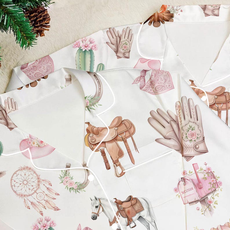 Puede incluir: Camiseta de pijama blanca con estampado de tem&aacute;tica Western. El patr&oacute;n incluye ilustraciones de sillas de montar, caballos, guantes, cactus y atrapasue&ntilde;os en tonos marr&oacute;n, rosa y verde. La camiseta tiene ribetes blancos y cuello.