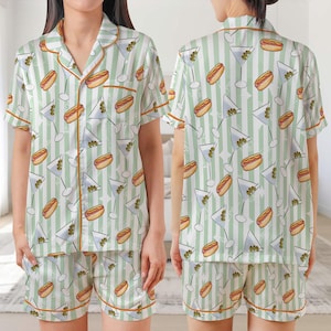 Könnte beinhalten: Ein zweiteiliges Pyjama-Set mit weißem und grünem Streifenmuster. Das Set besteht aus einem kurzärmeligen Hemd mit Knöpfen und passenden Shorts, die mit Martinigläsern und Hotdogs verziert sind. Die Kanten sind mit orangefarbenen Paspeln versehen.