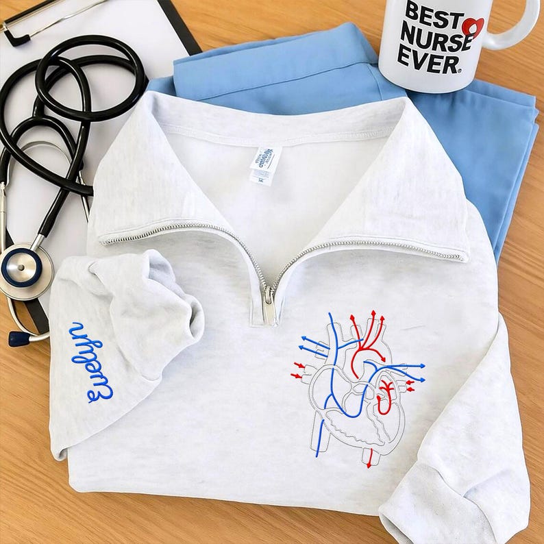 Personalized nurse quarter zip sweatshirt featuring an anatomical heart embroidery and custom name on sleeve. Soft fleece medical pullover, perfect gift for nurses, doctors, or healthcare professionals who love cozy, meaningful workwear.