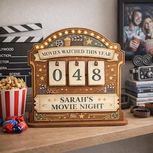 Könnte beinhalten: Holz-Filmnacht-Zähler mit dem Text "MOVIES WATCHED THIS YEAR" und "SARAH'S MOVIE NIGHT". Der Zähler zeigt die Zahl "048" an. Der Zähler ist mit Sternen, Filmrollen und Popcorn verziert.
