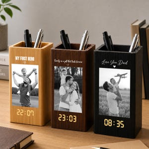 May include: Three rectangular wooden pen holders in light, medium, and dark finishes. Each features a black and white photo, a digital clock display, and engraved text: "MY FIRST HERO," "Family is a gift that lasts forever," and "Love You Dad."