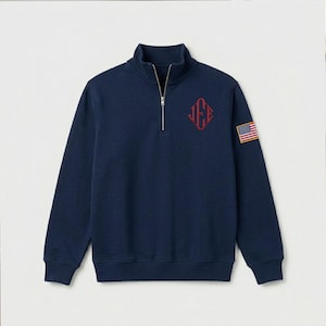 Puede incluir: Sudadera azul marino con cremallera de cuarto de cremallera y cuello alzado. Presenta un logotipo rojo bordado en el pecho y un pequeño parche de la bandera americana en la manga. Manga larga y dobladillo acanalado.