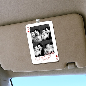May include: A white car visor card with a playing card design featuring four black and white photos of a couple. The card has a red heart and spade symbol, with the text "Drive safe! Baby I love you!" in red script.