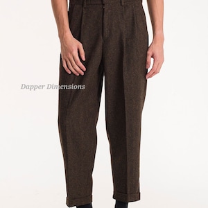 Könnte beinhalten: Braune Tweedhose mit Falten vorne und umgeschlagenem Saum. Die Hose wird mit schwarzen Schuhen kombiniert. Der Text "Dapper Dimensions" ist auf der linken Seite des Bildes sichtbar. Der Gesamtstil ist klassisch und maßgeschneidert.