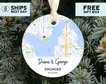 May include: A white round ornament with a map of Seattle, Washington. A red heart is placed on the map. The text "Diana & George ENGAGED 8/12/2022" is printed on the ornament.