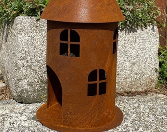 Könnte beinhalten: Ein rostiger Metallturm mit einem spitzen Dach und zwei Fenstern. Der Turm ist so konzipiert, dass er wie ein kleines Haus aussieht und hat eine abgerundete Öffnung an einer Seite.