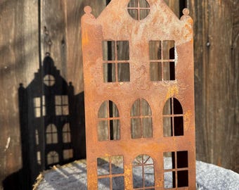 Könnte beinhalten: Ein rostiges Metallausschnitt eines Hauses mit mehreren Fenstern. Das Haus steht auf einem mit Schnee bedeckten Baumstumpf.