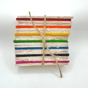 May include: A stack of colourful square coasters tied with twine. The coasters are in various colours, including red, orange, yellow, green, blue, black, and pink. The twine is wrapped around the stack, holding them together.
