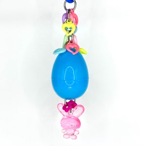 May include: A blue plastic Easter egg with a pink bunny charm hanging from it. The egg is decorated with colourful plastic hearts and beads.