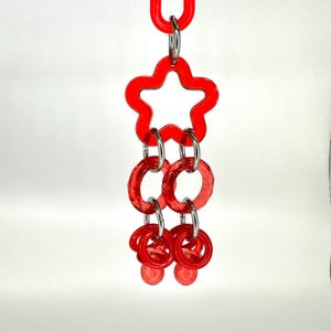 May include: Red plastic star-shaped toy with multiple linked rings hanging from it. The toy is designed for a bird to play with.