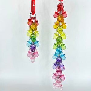 May include: Rainbow pacifier charm earrings with a silver chain and a red hook closure. The charms are made of clear plastic and are arranged in a rainbow pattern.