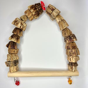 May include: A bird swing made from natural materials. The swing features a wooden dowel base and is suspended by a red metal clip. The sides are constructed from stacked, textured bark pieces, and it's decorated with colourful beads.