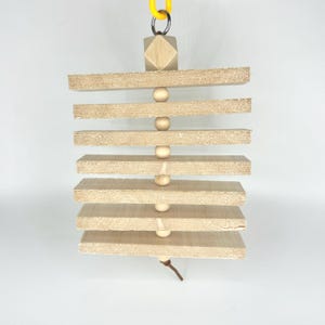 May include: A bird toy made of natural wood and wooden beads. The toy has several horizontal wooden planks held together by wooden beads. A yellow chain and a small wooden cube are at the top. A leather string hangs from the bottom.