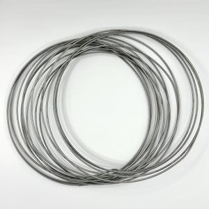 May include: A collection of thin, silver-coloured metal rings arranged in a circular pattern. The rings are overlapping and appear to be made of a flexible material. The background is plain white, providing a clean contrast to the metallic rings.