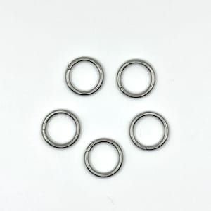 May include: Five silver jump rings, each with a small opening, arranged on a white background. The rings are circular and made of a shiny metal. They are likely used for jewellery making or crafts.