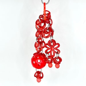 May include: A red plastic toy with a ball, flowers, and rings hanging from a silver loop.