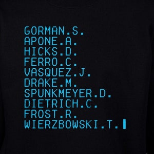 Può includere: Felpa nera con un font digitale blu che elenca i nomi in una colonna. I nomi includono Gorman, Apone, Hicks, Ferro, Vasquez, Drake, Spunkmeyer, Dietrich, Frost e Wierzbowski.