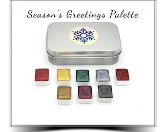 May include: A metal tin with a snowflake design on the lid. The tin contains a set of 10 watercolor paints in a variety of metallic colors. The colors include gold, silver, copper, and red. The tin is labeled "Season's Greetings Palette".