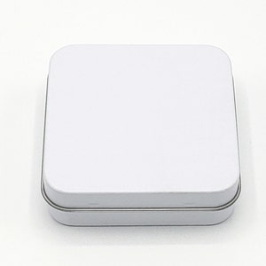 May include: A white square tin box with a silver rim.