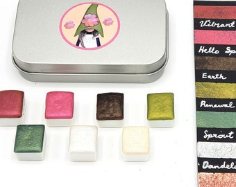 May include: A set of 8 metallic watercolor paints in a tin box with a gnome illustration on the lid. The paint colors are vibrant, hello spring, earth, renewal, sprout, dandelion, and abloom.