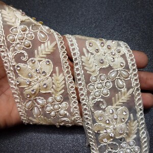 May include: White beaded and rhinestone trim with a floral design. The trim is made of sheer fabric and has a delicate, feminine look.