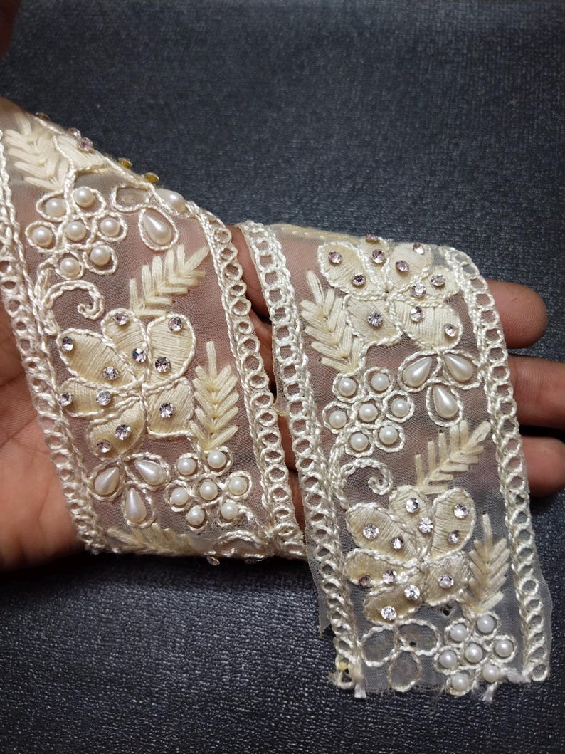 May include: White beaded and rhinestone trim with a floral design. The trim is made of sheer fabric and has a delicate, feminine look.