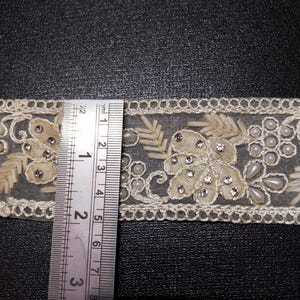 May include: White lace trim with pearl and rhinestone embellishments. The trim is approximately 2.5 inches wide.