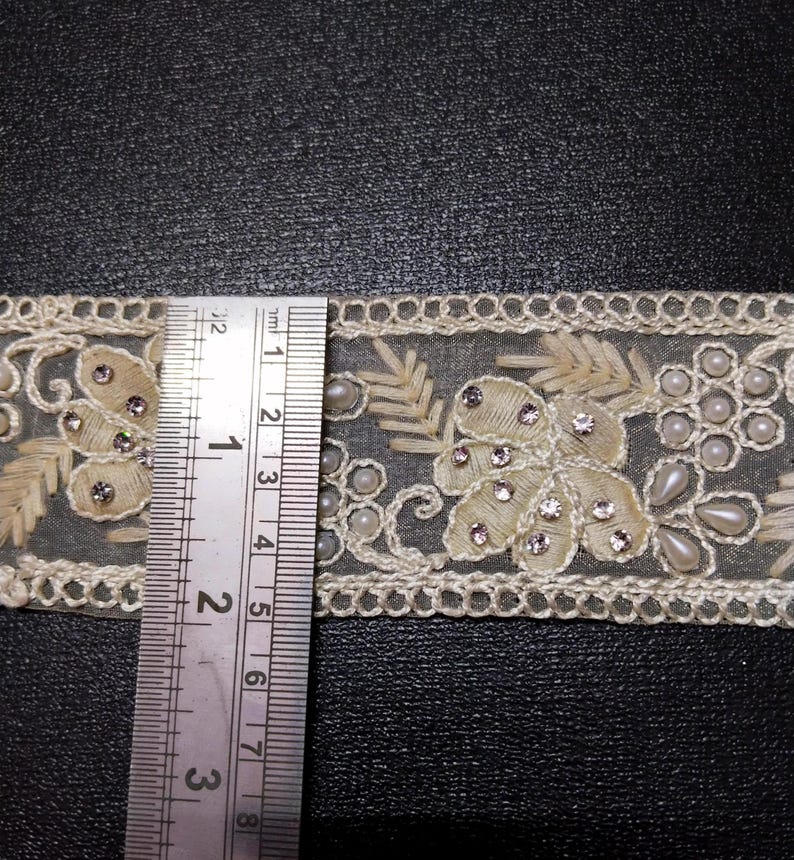 May include: White lace trim with pearl and rhinestone embellishments. The trim is approximately 2.5 inches wide.