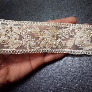 May include: White sheer lace trim with pearl and rhinestone embellishments. The trim features a floral design with delicate leaves and intricate details.