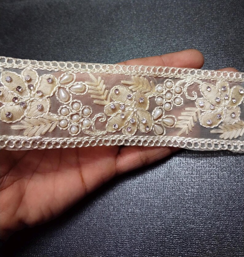 May include: White sheer lace trim with pearl and rhinestone embellishments. The trim features a floral design with delicate leaves and intricate details.