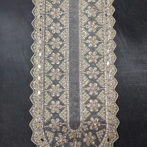 Puede incluir: Aplicación decorativa de tela blanquecina con intrincados patrones florales y geométricos. El diseño presenta perlas de imitación, lentejuelas y detalles reflectantes, creando un efecto brillante. Los bordes están festoneados, agregando un toque delicado.