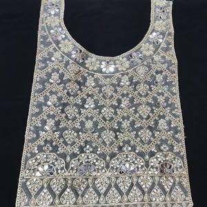 May include: A sheer, sleeveless garment overlay featuring a scoop neckline, adorned with intricate gold embroidery, reflective mirror accents, and small white beads arranged in a repeating chevron and floral pattern throughout the fabric.