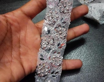 May include: Silver sequined trim with a floral design. The trim is made of a sheer fabric with silver sequins and rhinestones.