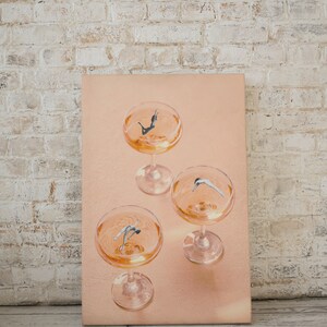 May include: Three champagne flutes filled with a pale orange liquid. Each flute contains a small figure of a person diving into the liquid.